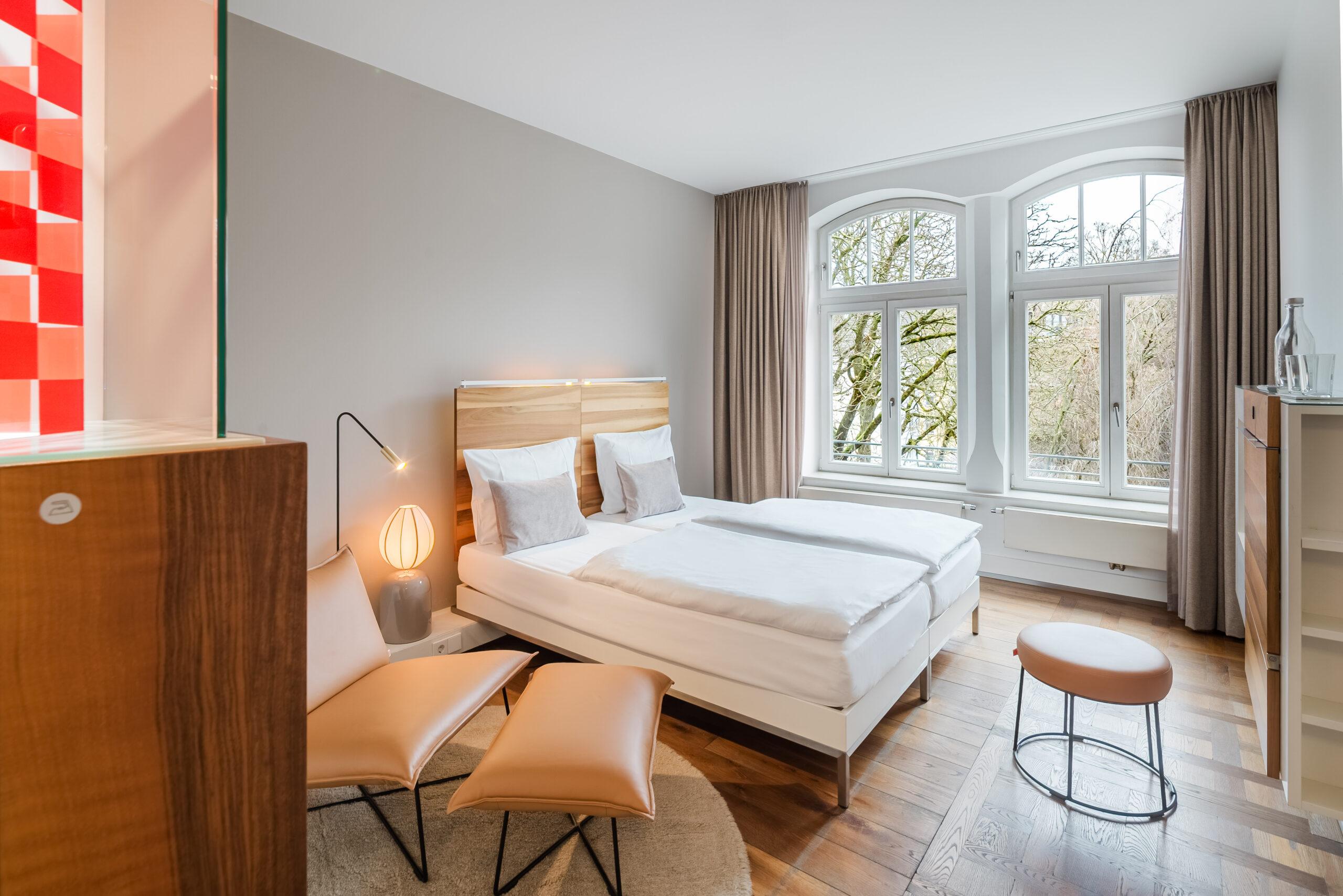 Helles Hotelzimmer mit Doppelbett, Sessel und Fensterblick.